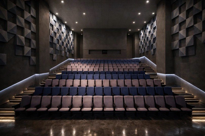 Multi-hall cinema with acoustic paneled walls, tiered seating, and ambient blue lighting